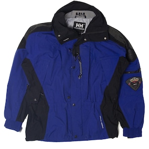 May include: Blue and black Helly Hansen jacket. The jacket features a high collar, a zipper closure, and multiple pockets. The sleeves have elastic cuffs. The jacket has the Helly Hansen logo on the chest and sleeve.