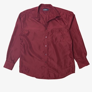 Può includere: Camicia bordeaux a maniche lunghe con bottoni e taschino sul petto. La camicia ha un colletto classico e polsini con bottoni. Il tessuto sembra lucido.