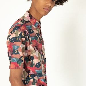 May include: A man wearing a short-sleeved button-down shirt with a colorful geometric print featuring cacti, mountains, and crescent moons.