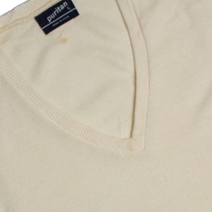 May include: Cream-colored V-neck sweater with a ribbed neckline and cuffs. The label reads "puritan" and "MADE IN U.S.A." The sweater is a size L. There is a small stain on the front of the sweater.
