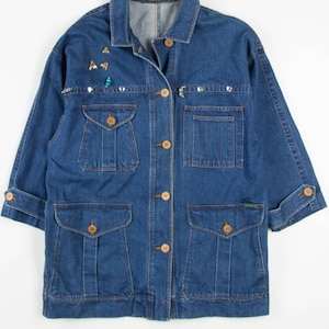 May include: A blue denim jacket with a button fastening and multiple pockets. The jacket has embellishments on the front, including small metal and plastic shapes.