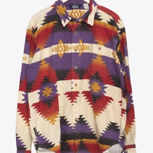 Puede incluir: Una camisa abotonada con un colorido estampado geométrico. La camisa presenta una base color crema con vibrantes acentos de rojo, morado, amarillo y negro. La camisa de manga larga está colgada en una percha de madera.