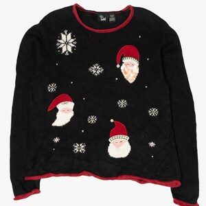 May include: Black Christmas jumper with red trim and Santa Claus faces. The jumper features white snowflakes and Santa faces with red hats and white beards. A festive holiday garment.