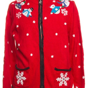 May include: Red zip-up sweater with white snowflake and snowman designs. The sweater has a black zipper and trim, and two front pockets with snowflake appliques. The snowmen are wearing hats and scarves.