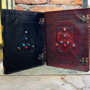 May include: Two leather-bound journals with intricate designs and Celtic knotwork. Each journal features a triquetra symbol adorned with colorful gemstones.