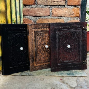 May include: Three leather-bound journals with intricate designs and a pentagram symbol. The journals are brown, black, and tan with a white stone embellishment on each cover.