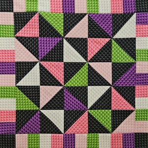 Pode incluir: Colcha geométrica texturizada com um padrão repetitivo. O design apresenta triângulos e quadrados em preto, branco, rosa, roxo e verde. A colcha tem uma superfície texturizada.