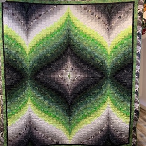 May include: A green and grey quilt with a diamond pattern. The quilt is made of fabric squares sewn together to create a geometric design.