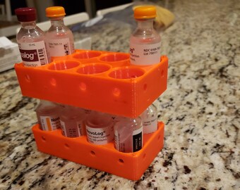 May include: Orange plastic vial organizer with multiple compartments. The organizer is holding several small glass vials with orange, red, and clear caps. The vials have labels with text including "NovoLog", "alog", and "NDC 0169.7501-11".