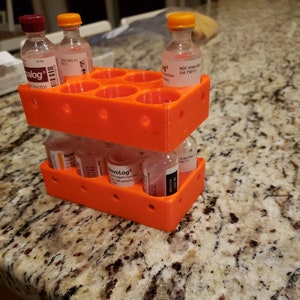 May include: Orange plastic vial organizer with multiple compartments. The organizer is holding several small glass vials with orange, red, and clear caps. The vials have labels with text including "NovoLog", "alog", and "NDC 0169.7501-11".