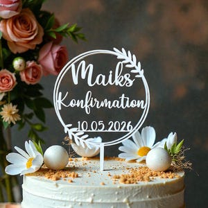 Könnte beinhalten: Eine weiße Torte mit einem Tortenaufsatz mit der Aufschrift "Maiks Konfirmation 10.05.2026". Die Torte ist mit weißen Gänseblümchen, weißen Kugeln und Krümeln verziert. Rosa Rosen und Grünzeug sind im Hintergrund.