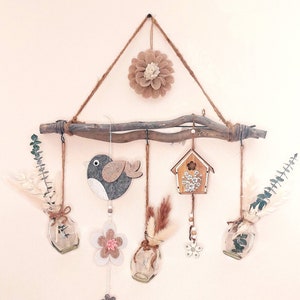 Könnte beinhalten: Ein rustikaler Ast aus Holz mit hängenden Dekorationen, darunter ein Vogel, ein Vogelhaus, Blumen und kleine Glasvasen mit Trockenblumen. Das Wort "Liebe" ist auf einem Holzsockel angebracht.