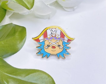 May include: A gold-colored enamel pin featuring a cartoon character with blue hair, a pirate hat with a skull and crossbones, and crossed swords. The pin has red, white, and yellow accents and is set against a white background.
