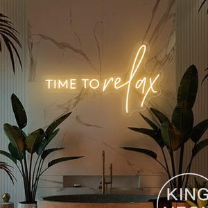Può includere: Un cartello al neon bianco con il testo "TIME TO relax" in un bagno con una vasca da bagno, piante e candele. Il cartello è illuminato da una calda luce gialla. Il testo "KING NEON" è visibile nell'angolo in basso a destra dell'immagine.