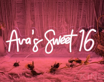 May include: Pink neon sign with white script that reads "Ava's Sweet 16". The sign is sitting on a fluffy pink rug in front of a wall with a woven texture.