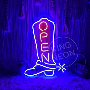 Pode incluir: Placa de néon em forma de bota de cowboy com a palavra "OPEN" em letras de néon rosa dentro da bota.