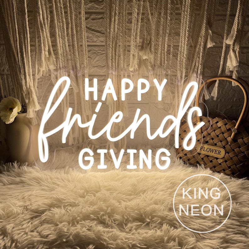 May include: A neon sign with the words "HAPPY FriendsGIVING" in white script. The sign is on a fluffy, cream-colored rug. A woven basket with a "FLOWER" tag and a vase with a flower are in the background. The sign also has the text "KING NEON".