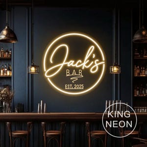 Op de afbeelding: Een cirkelvormig neonbord voor "Jack's Bar", oplichtend in een warmgele kleur. Het bord toont de naam van de bar in een sierlijk lettertype, het woord "BAR" en de oprichtingsdatum "EST, 2025".