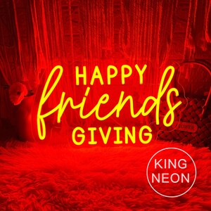 May include: A neon sign with the words "HAPPY friends GIVING" in yellow script. The sign is set against a red background, with a fluffy red surface below. The words "KING NEON" are in a white circle in the bottom right.