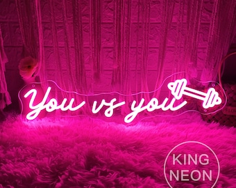 May include: White neon sign with the text "You vs You" and a dumbbell graphic. The sign is on a pink fuzzy surface. The text "KING NEON" is visible in the bottom right corner.