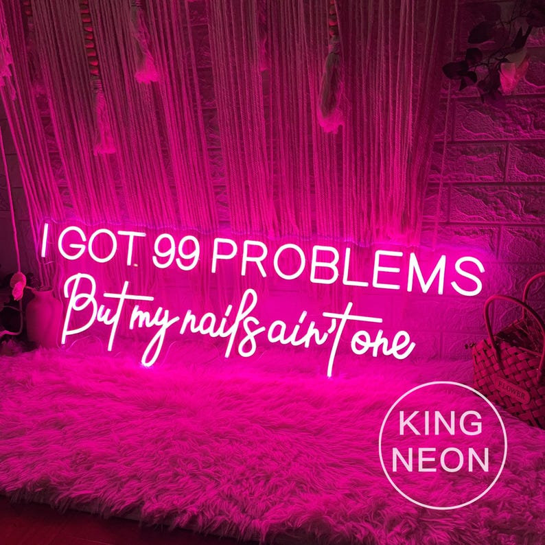 K&ouml;nnte beinhalten: Ein pinkfarbenes Neon-Schild mit dem Text "I got 99 problems but my nails ain't one". Das Schild leuchtet und h&auml;ngt an einer Wand mit einem wei&szlig;en und rosa Hintergrund. Das Schild wird von King Neon hergestellt.