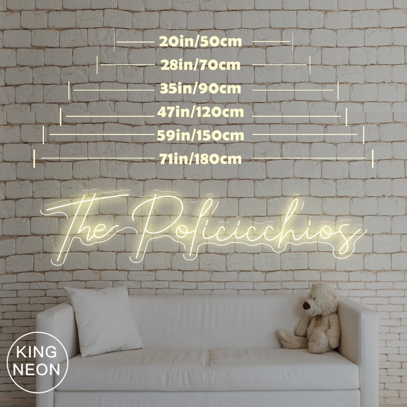 May include: White neon sign with the text "The Poficicchios" on a white brick wall. The sign is available in various sizes, ranging from 50 cm to 180 cm. The sign is displayed above a white sofa with a white throw pillow and a teddy bear.
