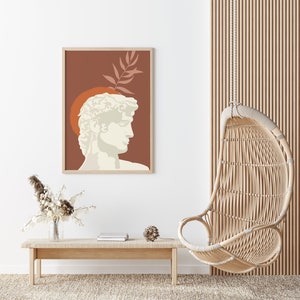 Pu&ograve; includere: Una stampa incorniciata di un busto bianco di un uomo con uno sfondo marrone e un design a foglia. Il busto &egrave; posizionato contro un cerchio rosso. La stampa &egrave; appesa a una parete bianca sopra un tavolo di legno con una sedia a dondolo in vimini sullo sfondo.