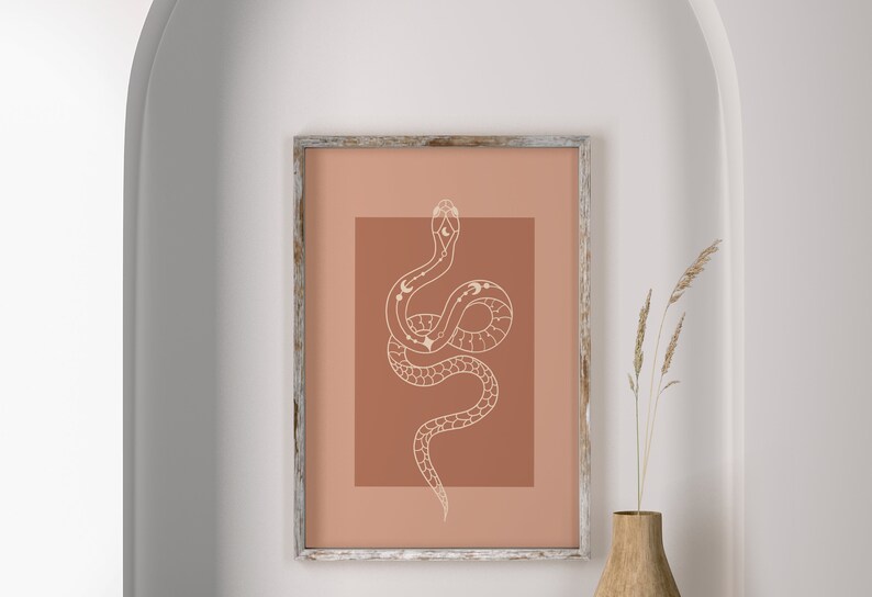 May include: A framed print with a minimalist design of a white snake with celestial symbols on a terracotta background.