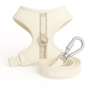 May include: Cream-colored dog harness and leash set. The harness features a snake-skin patterned accent and the text "PETSRUS". The leash has a silver metal clasp and the text "PETSRUS".