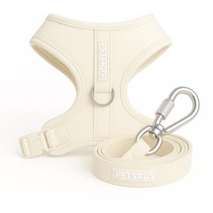 May include: A cream-colored dog harness and leash set with silver hardware. The harness has a D-ring and a buckle closure. The leash has a silver clip and the brand name "PETSRUS" is embossed on both the harness and leash.