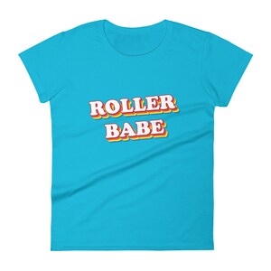 May include: A turquoise blue women's t-shirt with the text "ROLLER BABE" in a retro style font with red, yellow, and orange outlines.