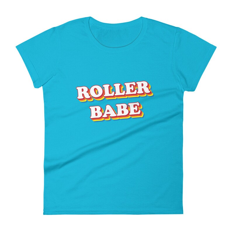 May include: A turquoise blue women's t-shirt with the text "ROLLER BABE" in a retro style font with red, yellow, and orange outlines.