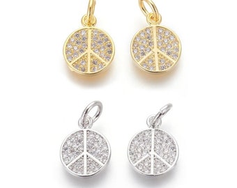 Puede incluir: Cuatro dijes con forma de signo de paz con detalles de cristal transparente. Dos dijes son dorados y dos son plateados.