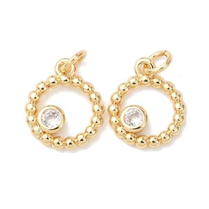 May include: Two gold-colored, round pendants with a beaded outer ring and a clear, round gemstone in the center. Each pendant has a small loop at the top for attaching to a chain or earring hook. The pendants are displayed against a white background.