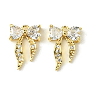 May include: A pair of gold-colored bow-shaped earrings. Each earring features a large, clear, pear-shaped stone at the top, with smaller clear stones set along the bow's curves. The earrings are set against a white background.