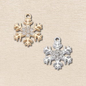 May include: Two snowflake charms, one in a gold tone and one in a silver tone, each featuring a central cluster of clear, round-cut crystals. Both charms have a small circular loop at the top for attachment and a six-pointed geometric design.