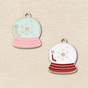 May include: Two metal snow globe charms with gold-tone edges and a small loop at the top. One charm features a light blue globe with a pink base and a white snowflake. The other charm has a white globe with a red base and a white snowflake.