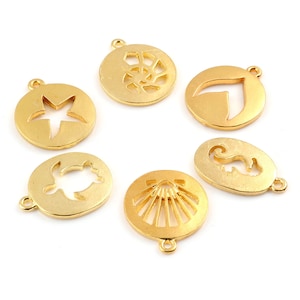 Peut inclure: Un ensemble de six breloques en métal doré présentant des motifs découpés sur le thème de l'océan, incluant une étoile de mer, un coquillage en spirale, une queue de baleine, une tortue marine, un coquillage en éventail et un hippocampe.