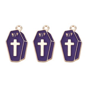 May include: Three purple coffin-shaped charms with gold trim. Each charm features a white cross and the letters "RIP" at the top. These Halloween-themed charms are perfect for jewelry making or crafting.