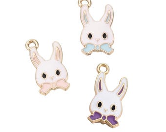 May include: Three gold-colored metal charms shaped like rabbit faces with different colored bows. The charms are white with black eyes and pink, purple, and blue bows.
