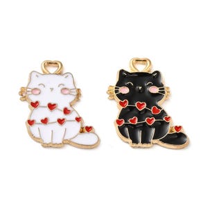 May include: Two gold-tone charm pendants featuring a black cat and a white cat with red hearts. Both cats are wearing a string of red hearts around their necks.