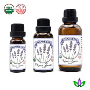 Może przedstawiać: Trzy brązowe szklane butelki olejku lawendowego z czarnymi zakrętkami. Każda butelka ma etykietę z napisem "Lavender Oil" i ilustracją gałązki lawendy. Butelki są oznaczone "Organic Zamara" i rozmiarami 15 ml, 30 ml i 60 ml.
