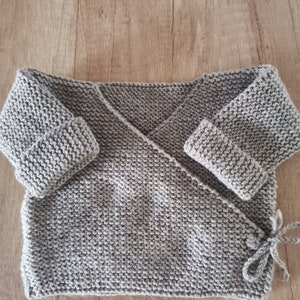 Puede incluir: Envoltura de bebé de punto gris con mangas largas y un lazo en la cintura.