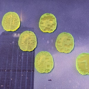 May include: Six translucent, neon green brain-shaped tokens. The tokens are arranged on a blue surface with a cityscape design. The brain tokens have detailed vein patterns and a glowing edge. The tokens are likely for a board game.