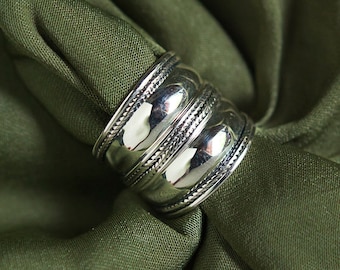 Könnte beinhalten: Ein silberner Ring mit einem strukturierten, mehrschichtigen Design. Der Ring wird auf einem grünen Stoffhintergrund präsentiert.