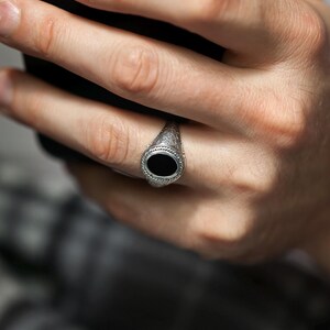 May include: A silver ring with a black oval stone set in a decorative band.
