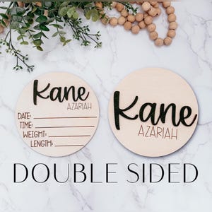 May include: Two double-sided wooden baby announcement signs. One side features the name "Kane Azariah" in black script, the other side has the name and space to write the date, time, weight, and length. The text "DOUBLE SIDED" is below.