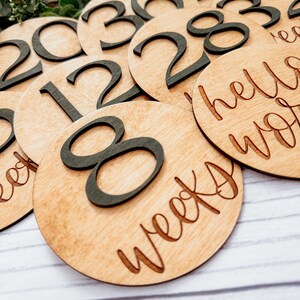 May include: Wooden circles with black numbers from 1 to 40 and the text "weeks" and "hello world". These circles are used to track pregnancy weeks.