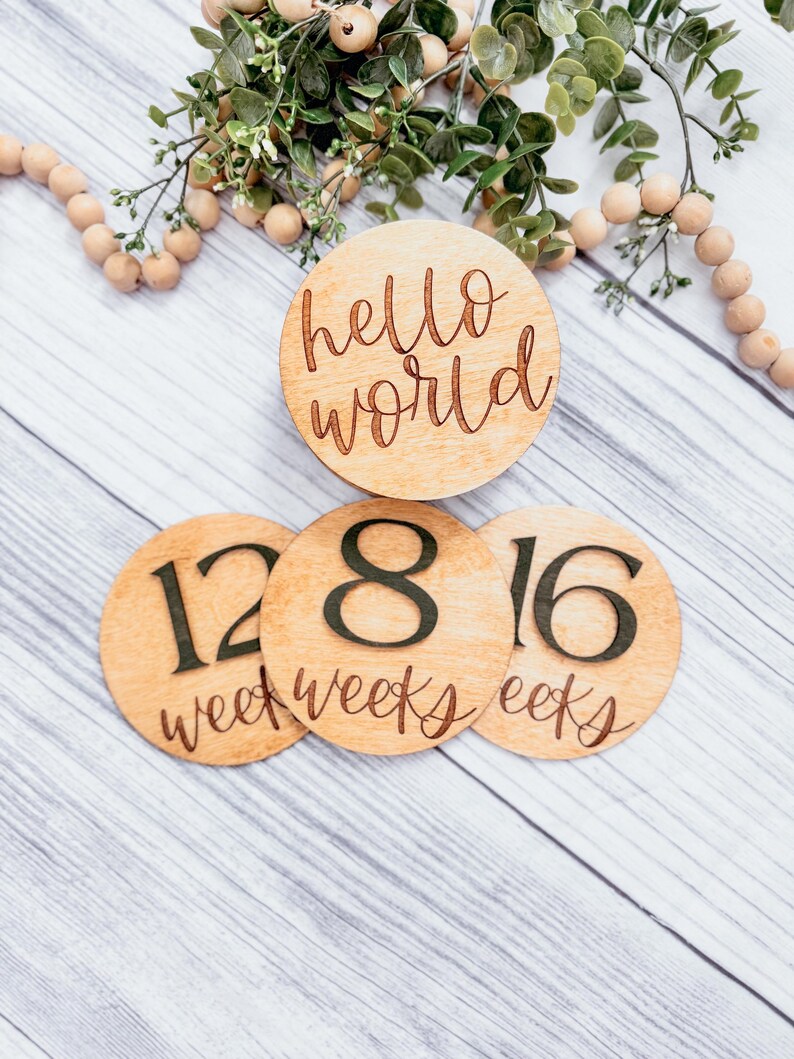 May include: Three wooden circles with the words "hello world", "12 weeks", "8 weeks", and "16 weeks" written on them. The circles are arranged in a triangle shape on a white wooden background.