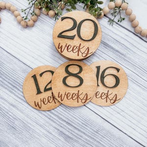 May include: Three wooden circles with numbers and the word "weeks" written on them. The numbers are 12, 18, and 20. The circles are stacked on top of each other.